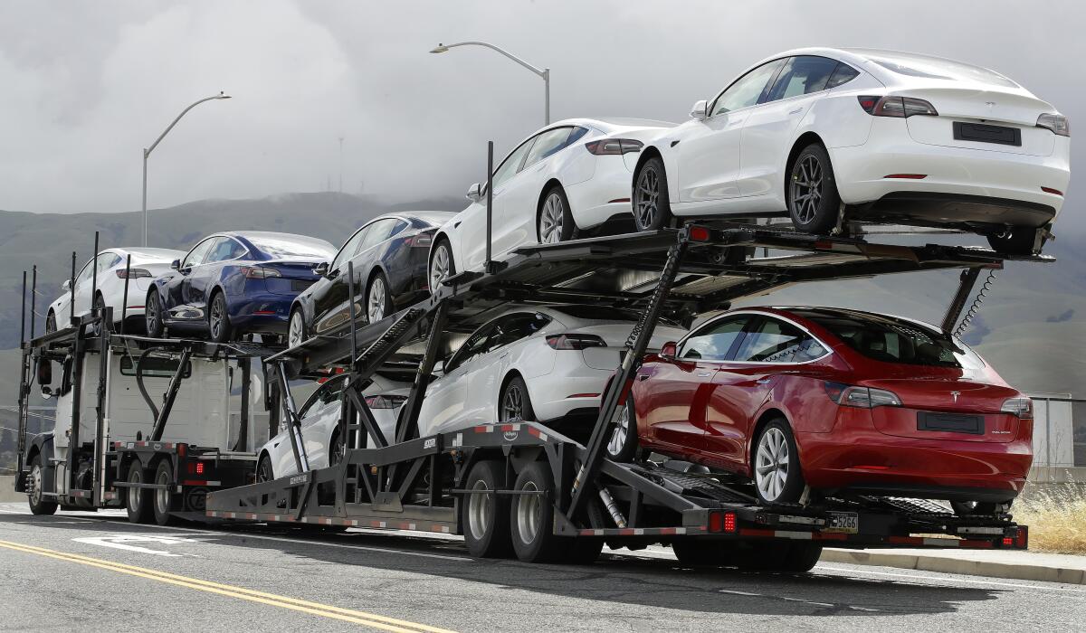 A car-carrying truck hauls eight new Tesla sedans down a highway.