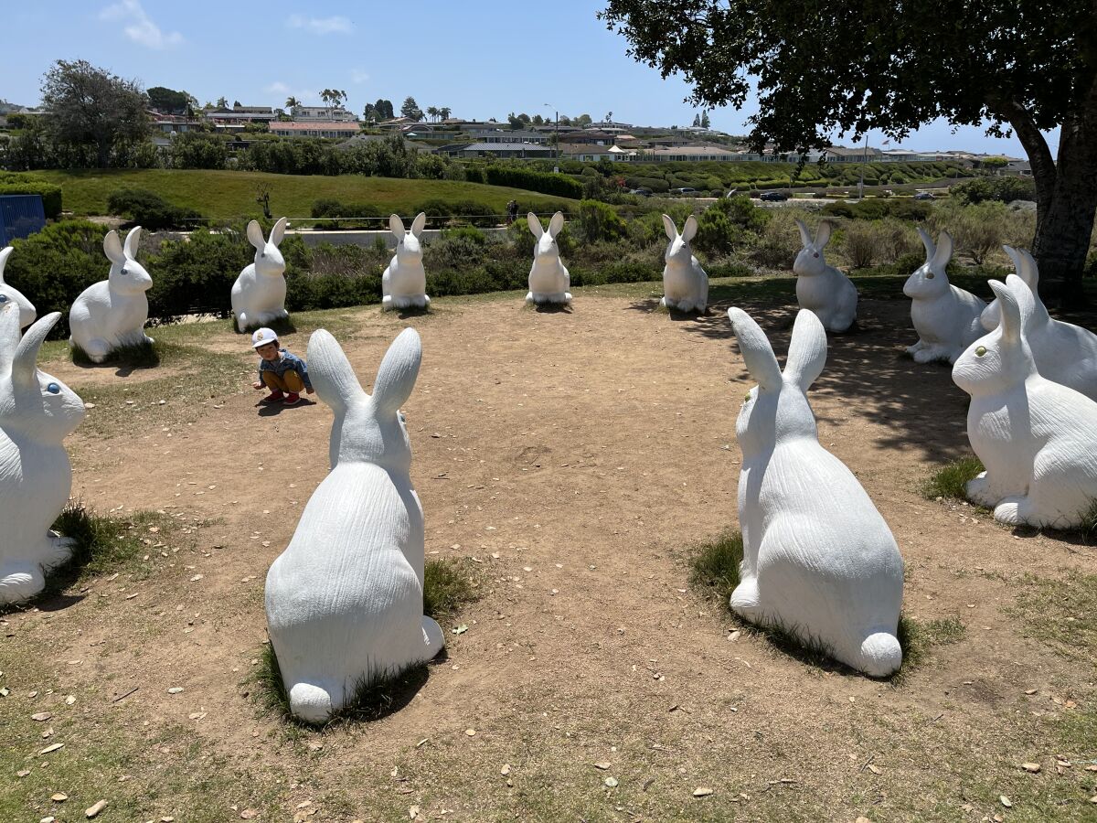 A circle of large white rabbit statues with a child crouched down toward the center.