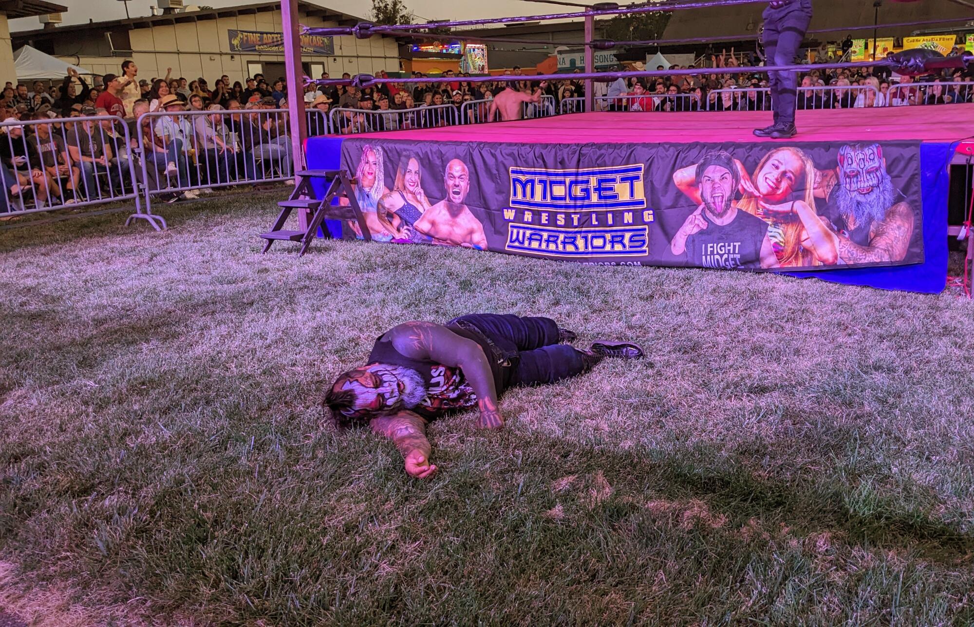 A person lies on the ground next to a wrestling ring.