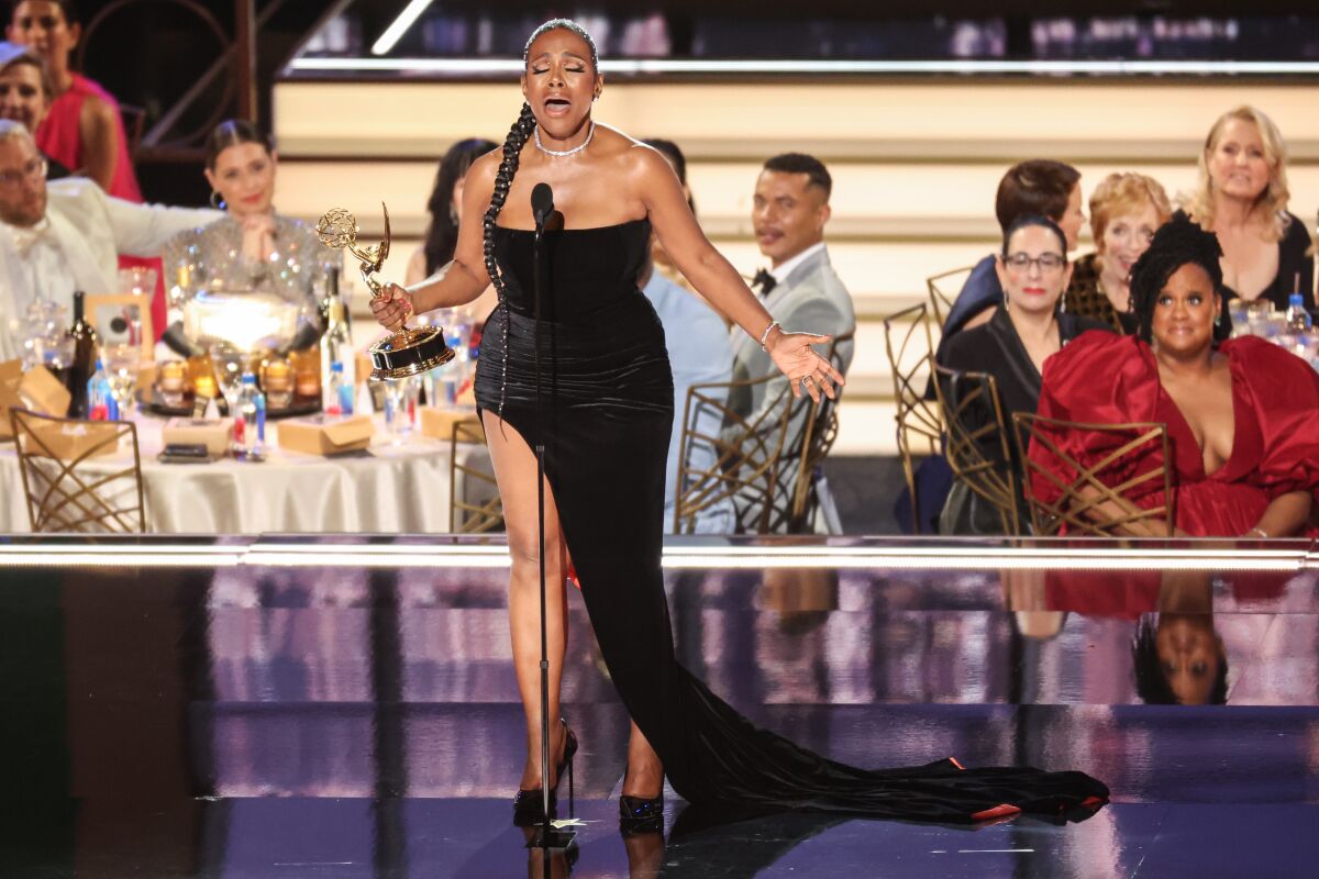 A woman in a long black gown sings on a stage while holding a gold trophy