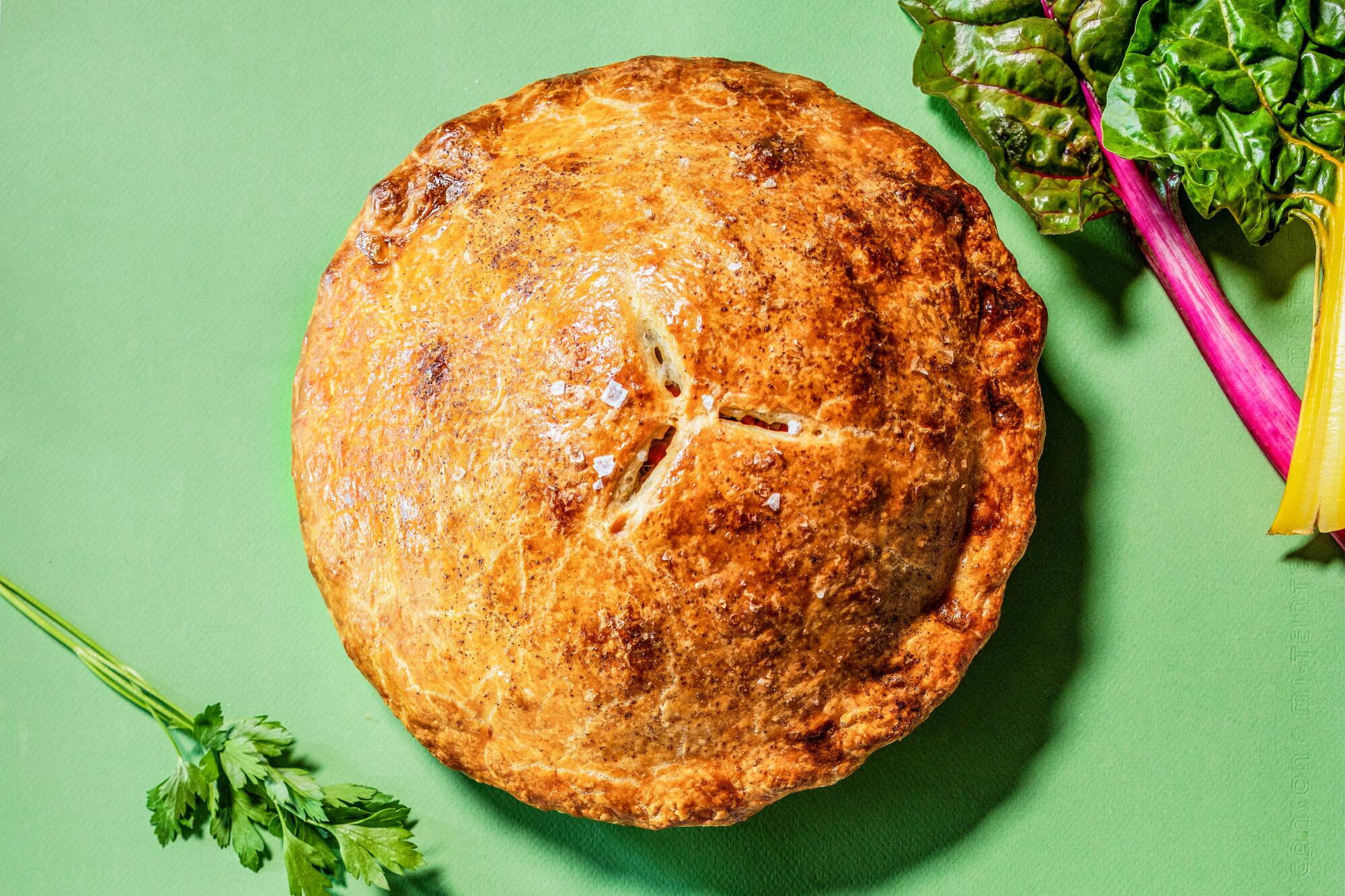 A chicken potpie with a sprig of parsley and a stalk of chard.