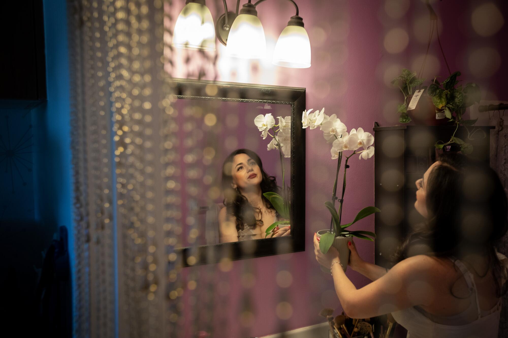 Gogo Akopyan holds potted flowers in front of her bathroom mirror