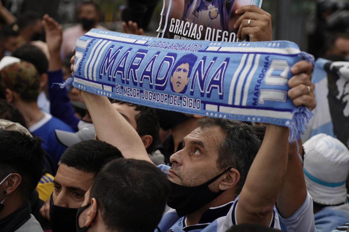 Amid a dense crowd of mourners, man holds up a Diego Maradona scarf.