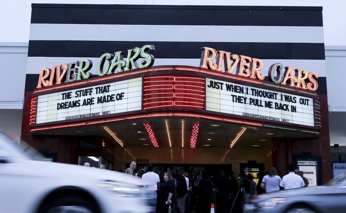 Cars drive by as media and attendees gather around the River Oaks Theater during a press conference announcing the small movie theater reopening in Houston on Wednesday, Feb. 2, 2022. (Elizabeth Conley/Houston Chronicle via AP)