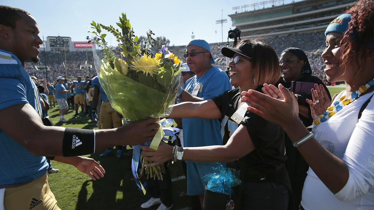 UCLA quarterback Brett Hundley, left, gives a bouquet of flowers to his mother, April, while greeting his family during the Bruins' senior day ceremony at the Rose Bowl on Nov. 28.