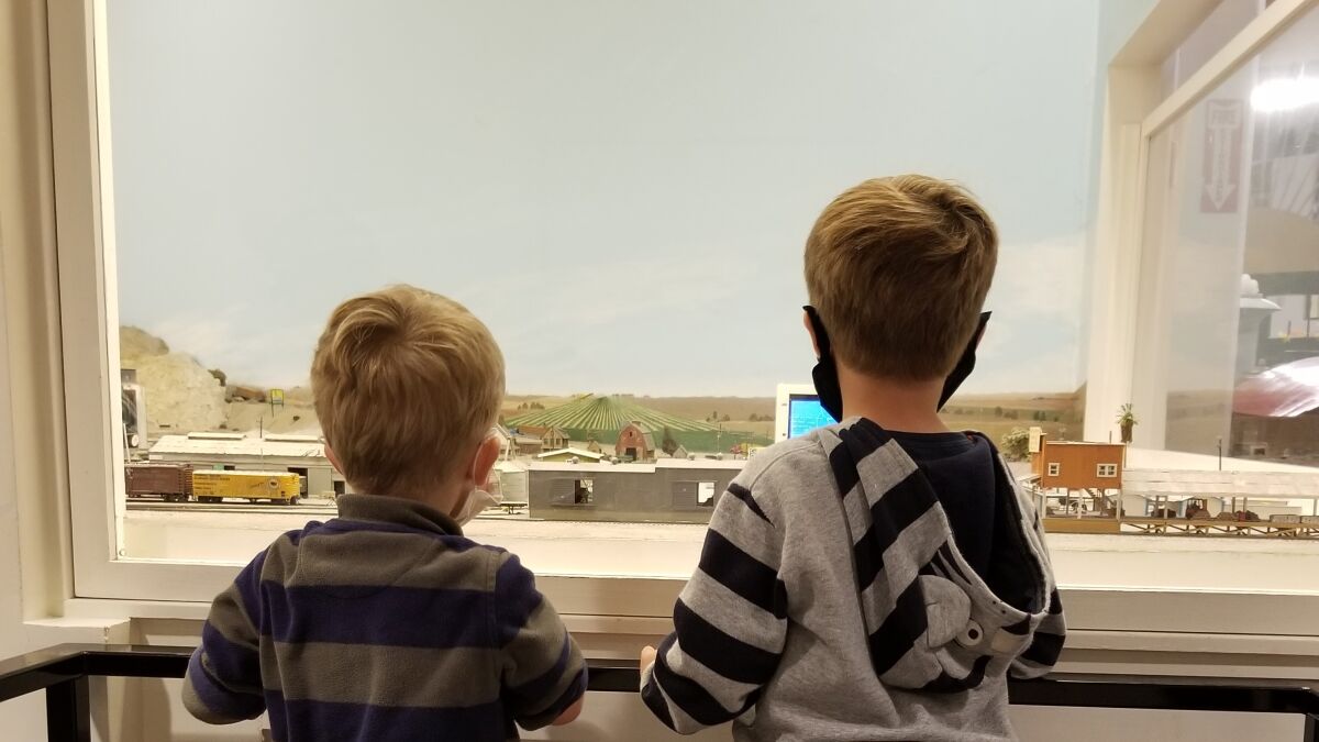 Two boys in masks admire a train layout at the San Diego Model Railroad Museum 