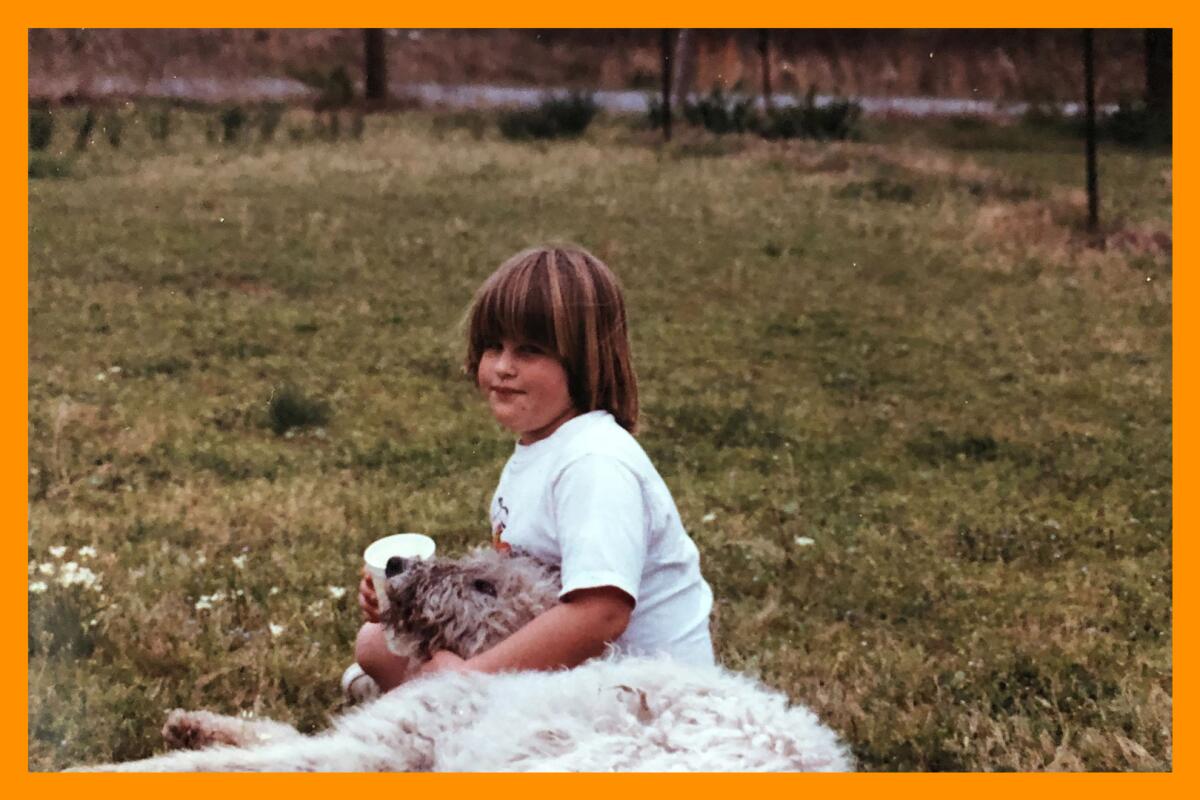 A child sits in a field with their arm around a dog
