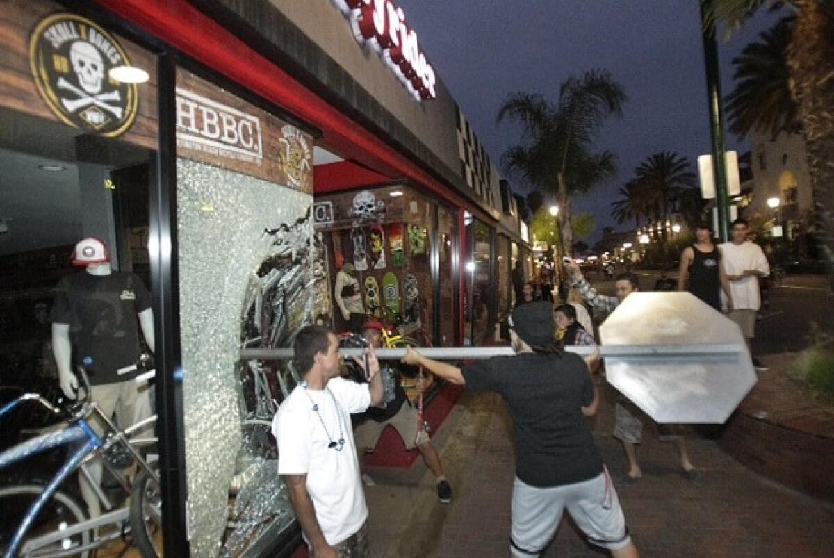 A rioter smashes a stop sign through the windows of Easyrider business on the corner of Main and Orange streets downtown Main Street in Huntington Beach following the US Open of Surfing contest finals. A few rioters looted a bike and other items from the store.