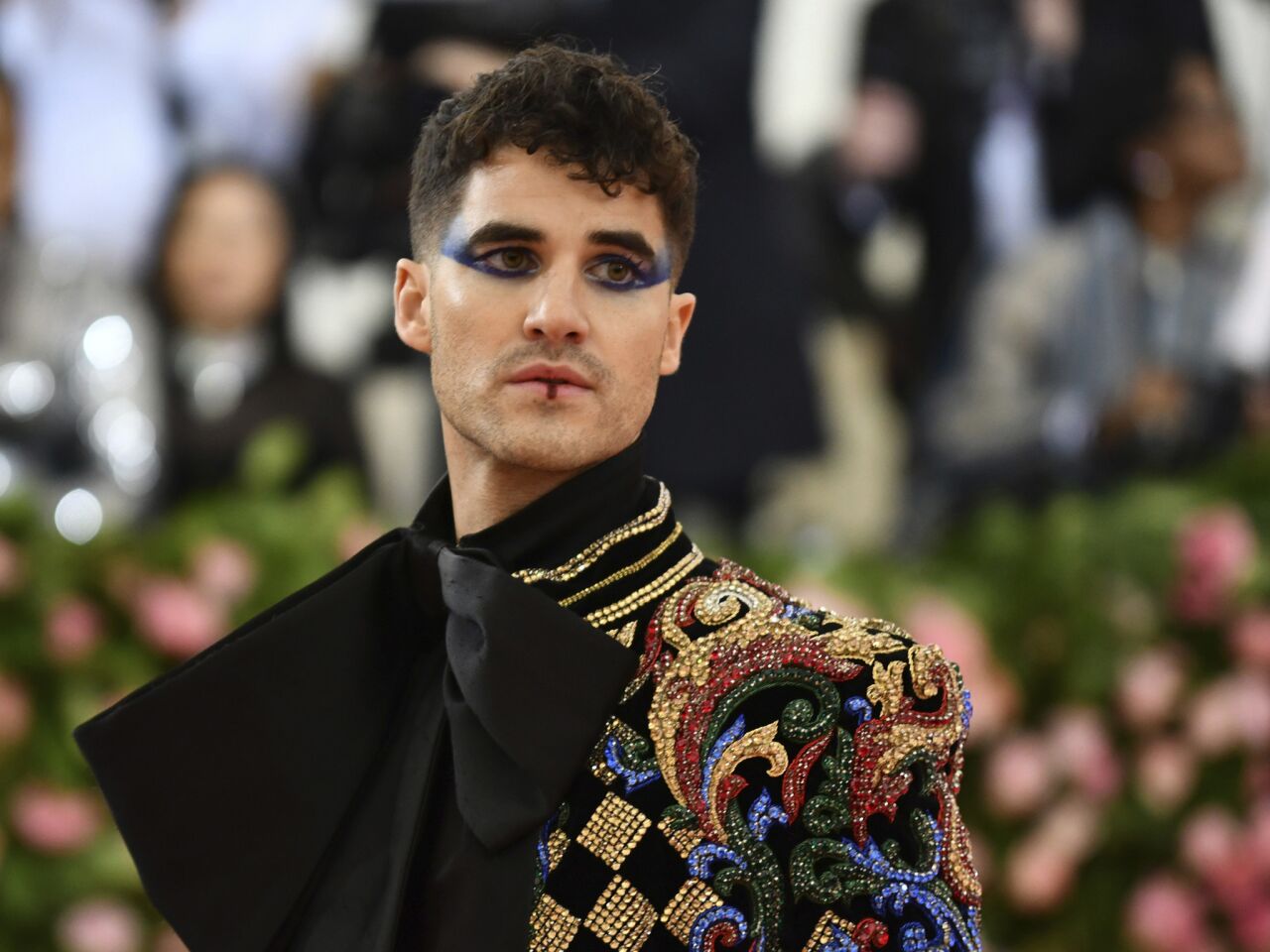 Actor Darren Criss wears a harlequin jacket and dramatic eye makeup for this year's Met Gala.