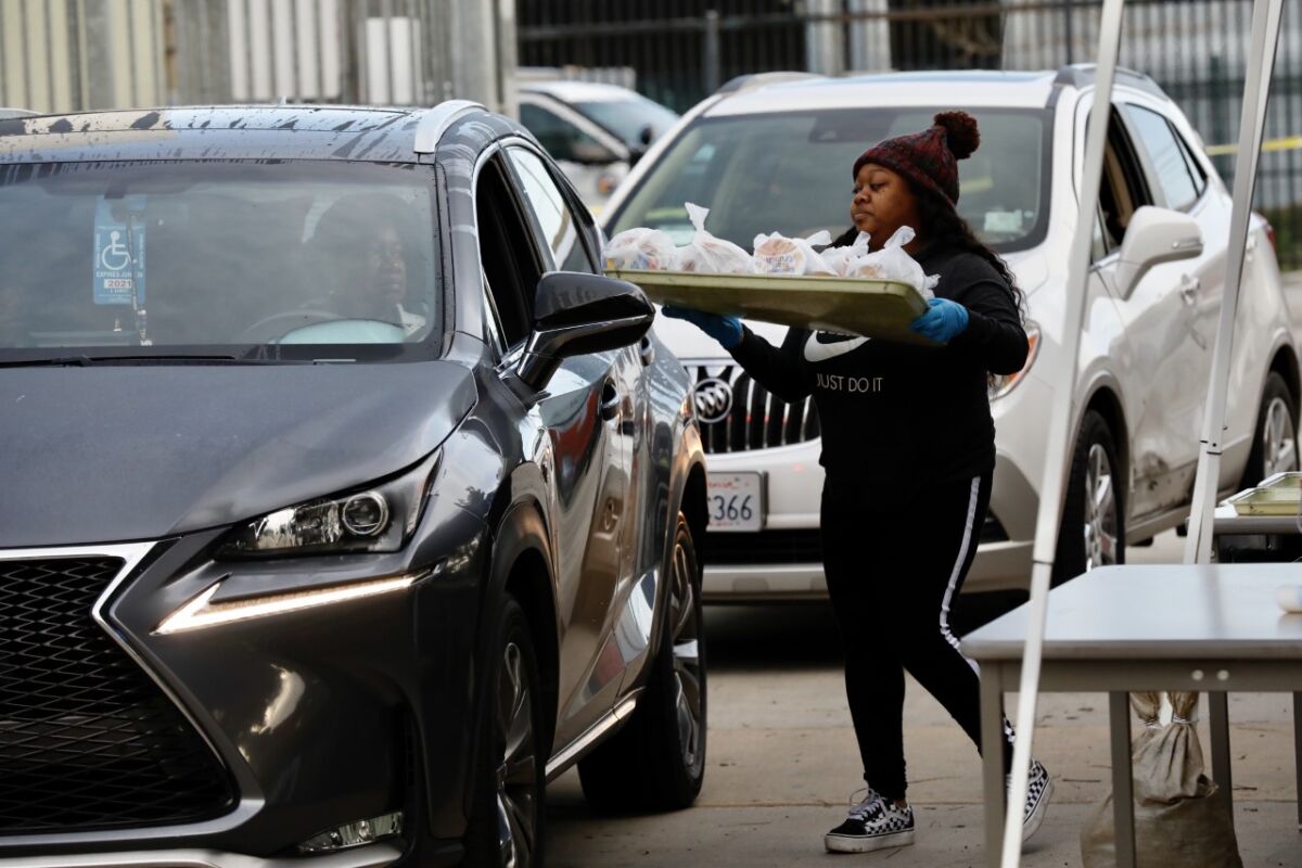 LAUSD volunteer Courtney Johnson delivers food to vehicles at Dorsey High School in Los Angeles this month. Pasadena schools have suspend their grab-and-go program after a kitchen worker fell ill.