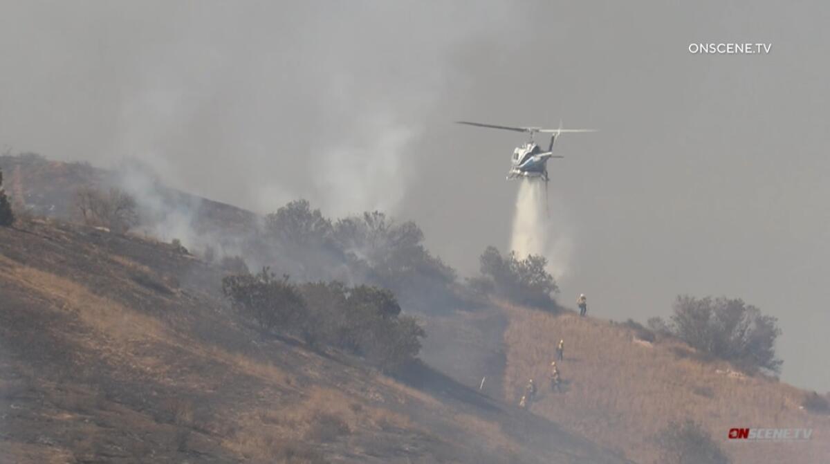 Firefighters work along the edge of a burn area as a helicopter drops water on the blaze Tuesday near Dehesa.
