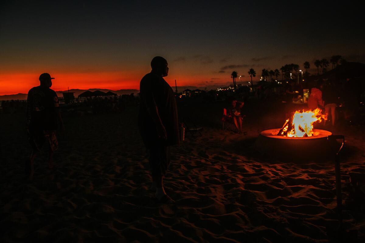 Dockweiler Beach at night while people gather around a fire pit.