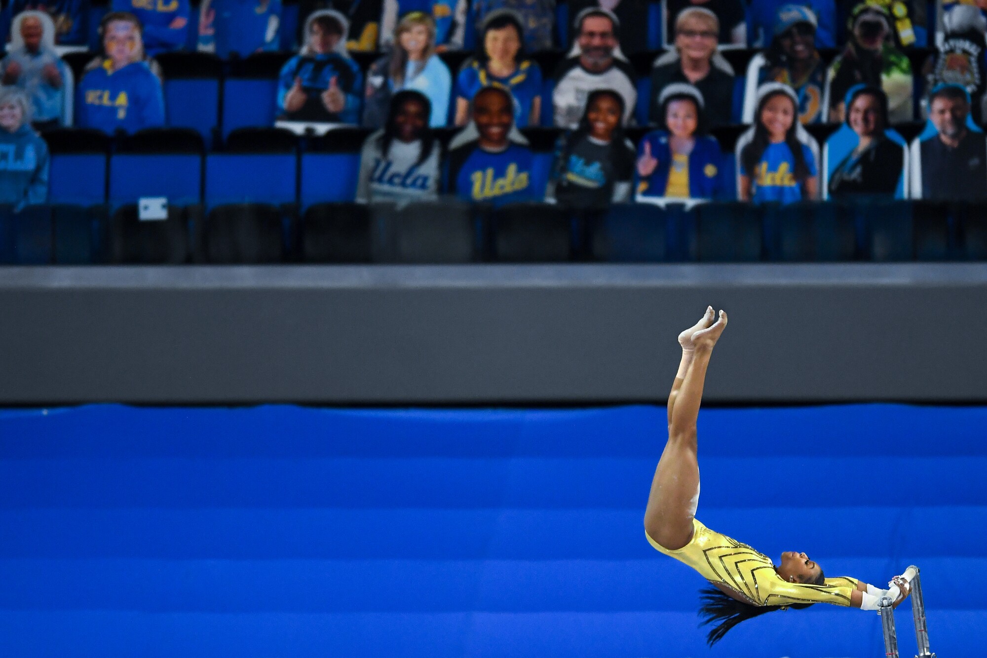 A gymnast in yellow competes on the uneven bars.