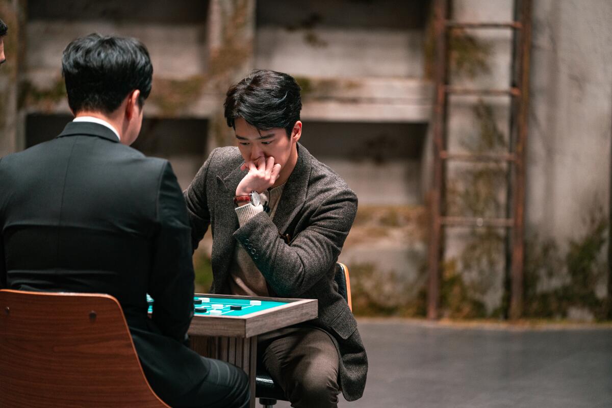 Two men in suits concentrate on a backgammon-like game.