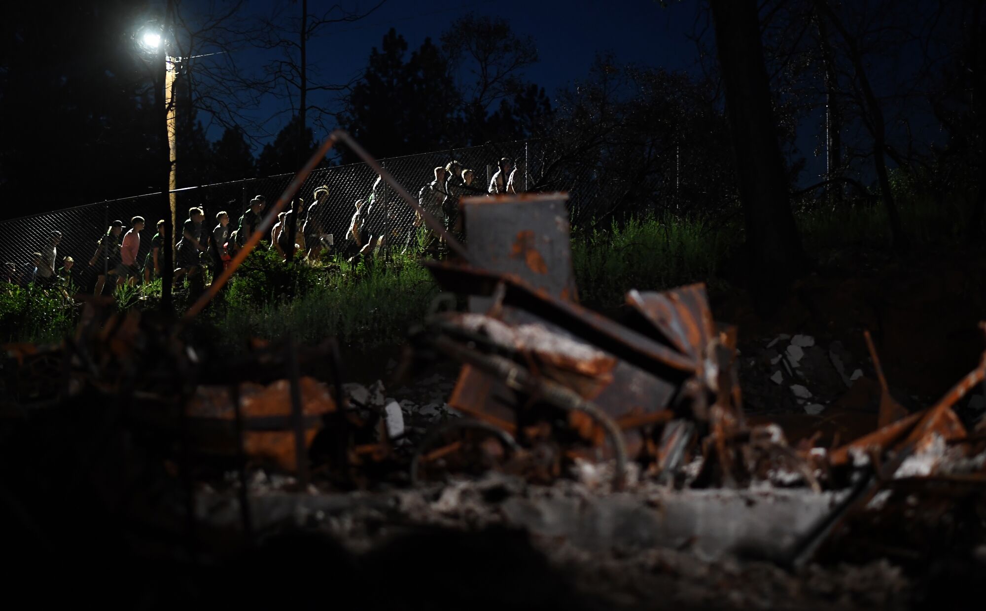 Paradise football players walk past burned structures while making their way up "Glory Hill" during a night training camp session.