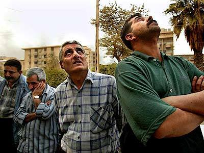 Iraqi men watch and listen as an American B-52 bomber flies over Baghdad on Tuesday. They say they will never accept the American invaders of their country.