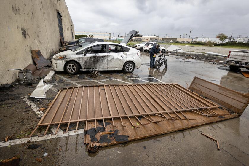 Montebello, CA - March 22: An employee who was inside the the Royal Paper Box Company when the roof was torn off during a strong microburst -- which some witnesses dubbed a possible tornado -- removes his bike from his damaged car at the scene where one person injured nearby and heavily damaged several cars and buildings, including the roof of the Royal Paper Box Company in Montebello Wednesday, March 22, 2023. Five buildings have been damaged and one has been red-tagged. Video from the scene showing portions of rooftops being ripped off industrial structures and debris swirling in the air. The National Weather Service on Tuesday night issued a brief tornado warning in southwestern Los Angeles County, but it was allowed to expire after about 15 minutes when weather conditions eased. There was no such warning in place late Wednesday morning when the powerful winds hit Montebello, near the area of Washington Boulevard and Vail Avenue. (Allen J. Schaben / Los Angeles Times)