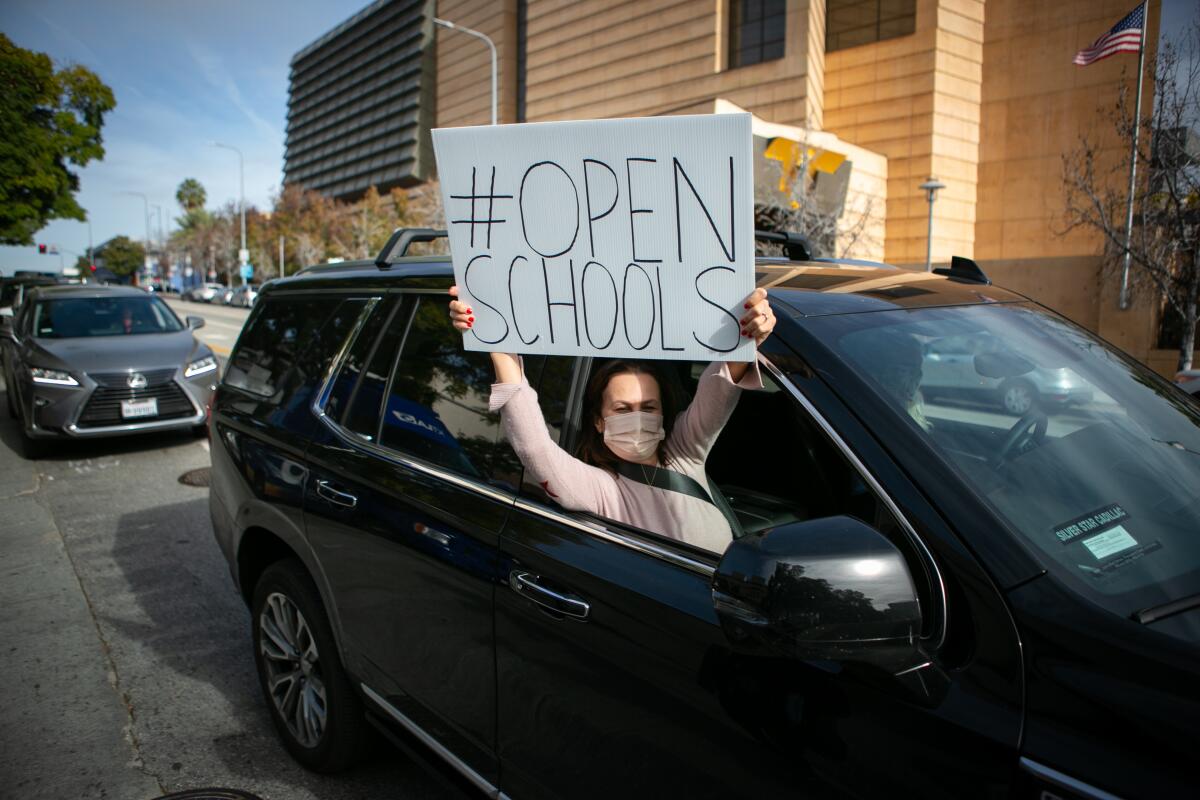 People in car caravan hold signs and honk horns at rally to open schools.