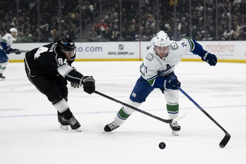 Vancouver Canucks left wing Nils Hoglander (21) and Los Angeles Kings defenseman Vladislav Gavrikov (84) vie for the puck during the first period of an NHL hockey game, Tuesday, March 5, 2024, in Los Angeles. (AP Photo/Kyusung Gong)