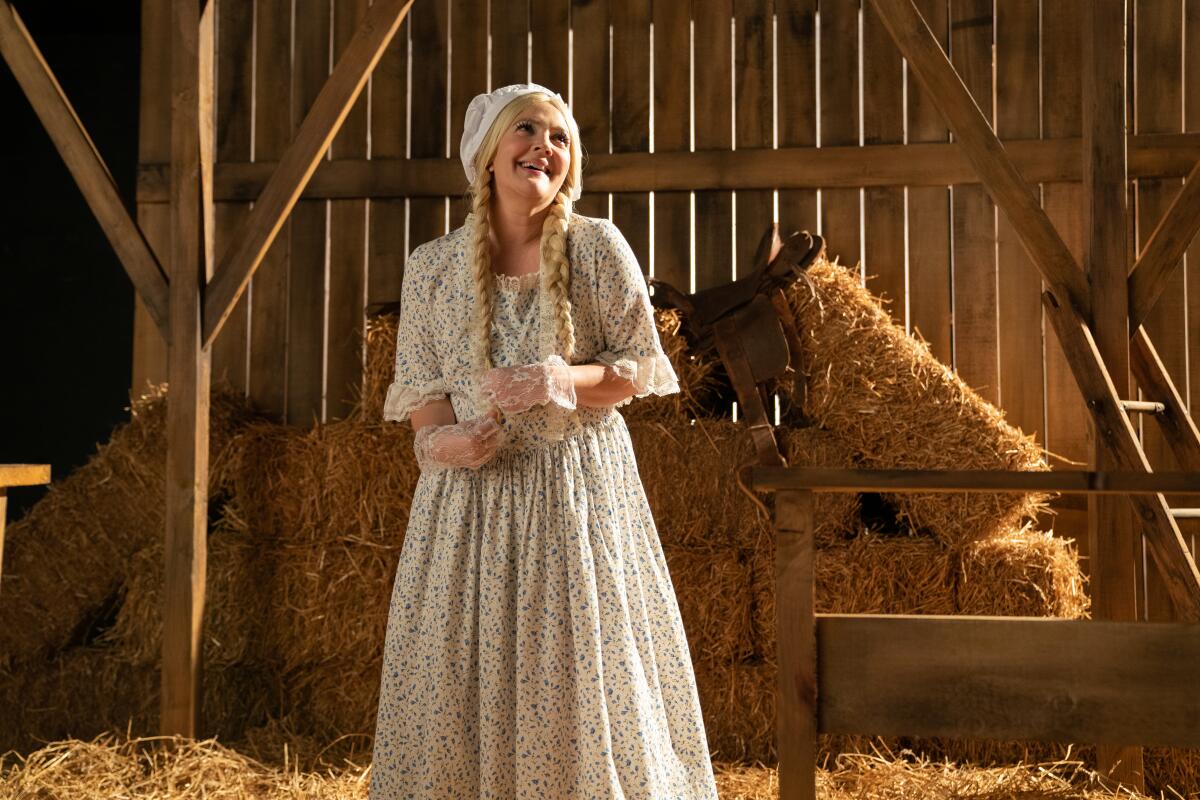 Drew Barrymore stands amid hay bales in a barn, wearing a long dress, gloves and bonnet, in "The Stand In."