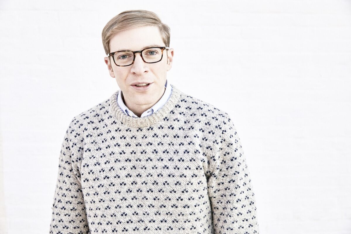A portrait of a man wearing a patterned sweater and glasses