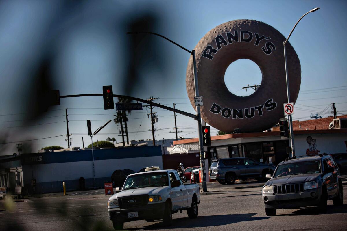 Vehicles drive near a shop with a giant donut on top 