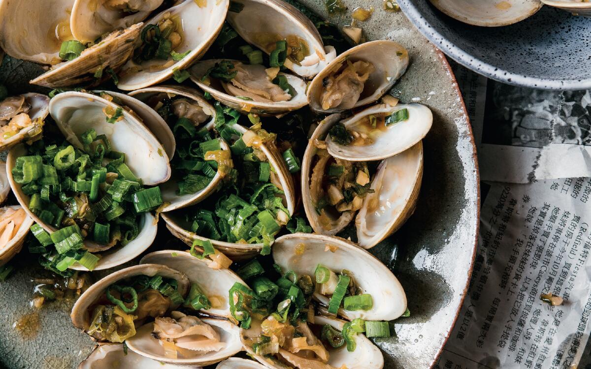 A plate of clams with chopped scallions sits atop Chinese-language newspapers.
