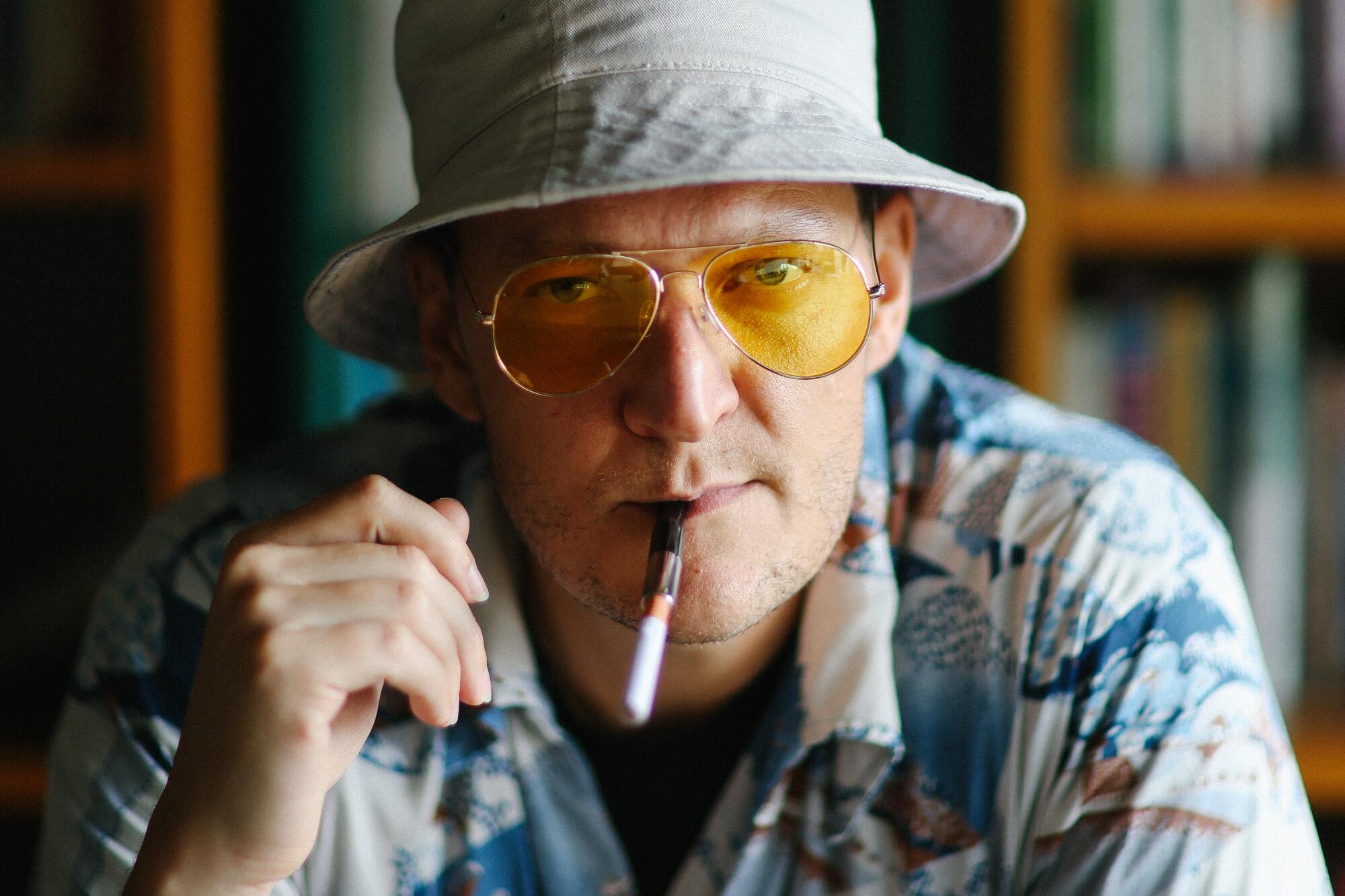 A man in a hat and sunglasses, with a cigarette holder in his mouth