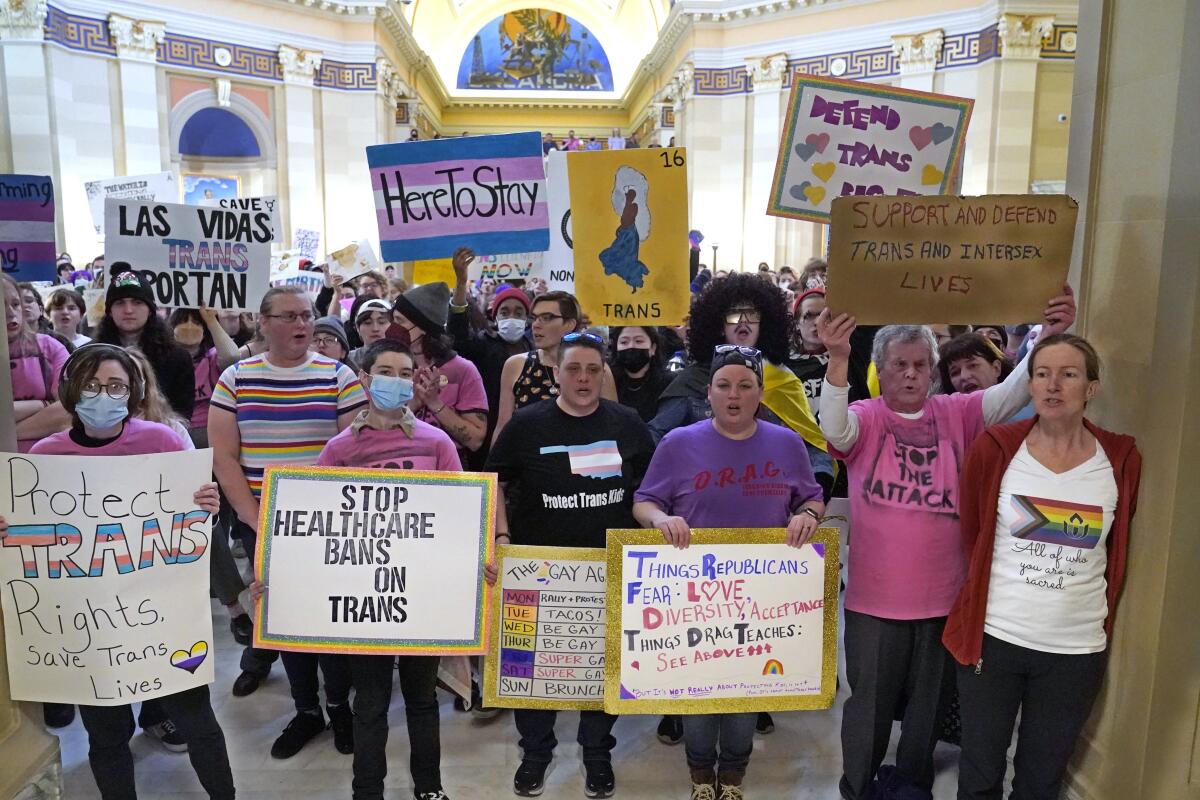 People hold signs reading "Protect Trans Rights" and "Stop Healthcare Bans on Trans."