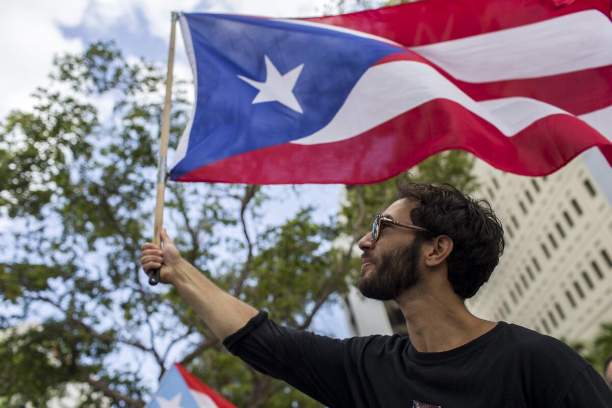 A man in a black shirt waves the flag of Puerto Rico, which is a single star in a blue triangle with red and white stripes