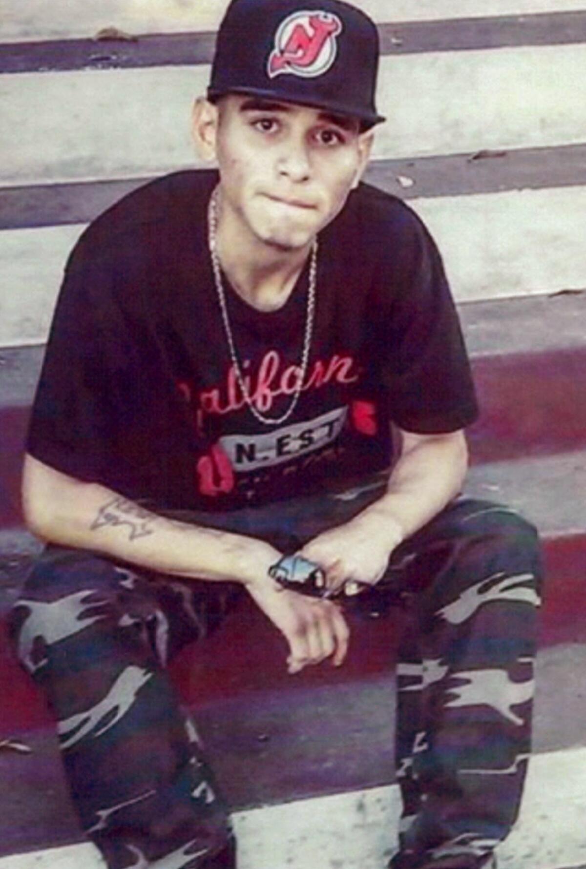 Carlos Rios seated on steps with camouflage pants, a black T-shirt and a New Jersey Devils baseball cap
