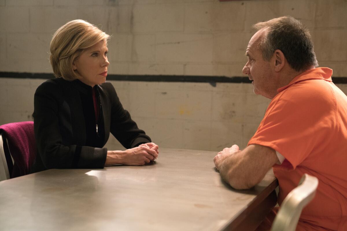 A woman in a dark suit jacket sits at a metal table in prison with a man in an orange jumpsuit.
