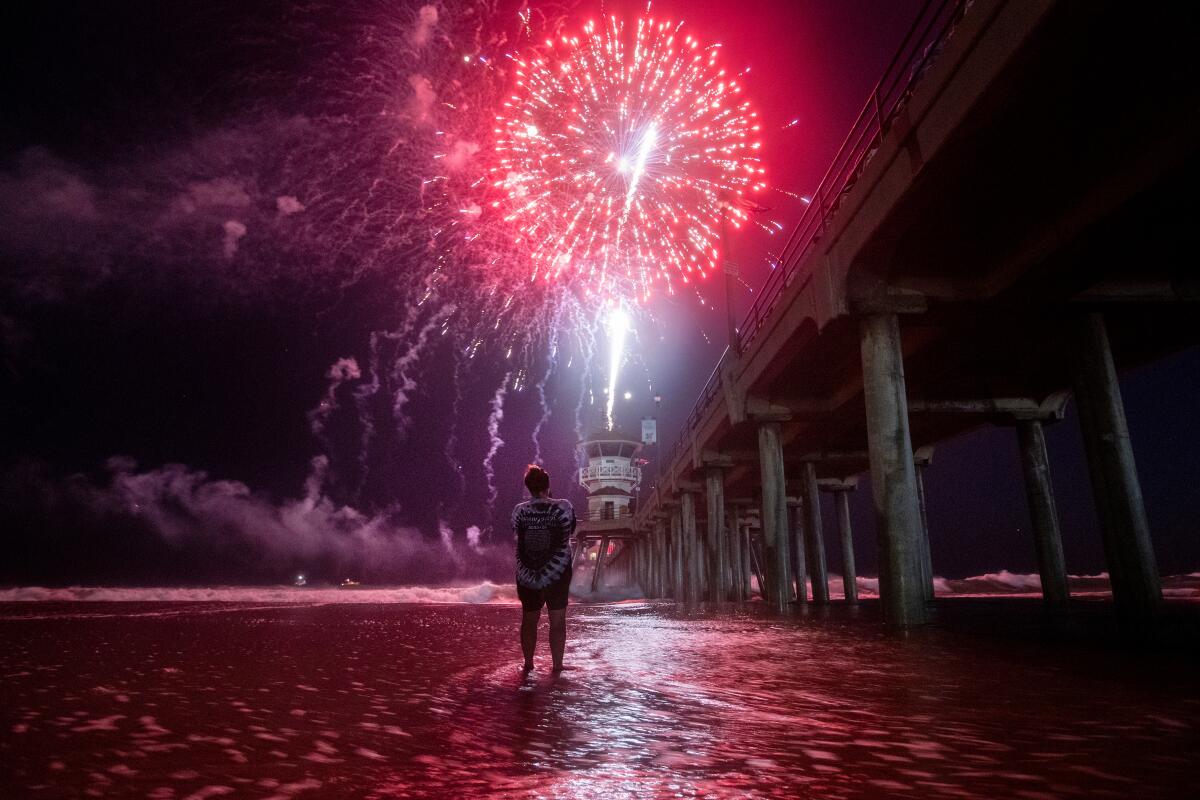 A person stands in the water by the Huntington Beach pier to watch fireworks.