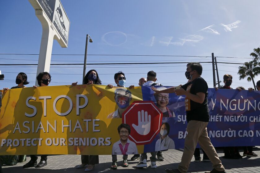 A group gathers in front of Whale Spa Salon Furniture on Friday holding a large banner as an airplane skywrites ONo HateO at the end of a Nailing It For America press conference in Huntington Beach.