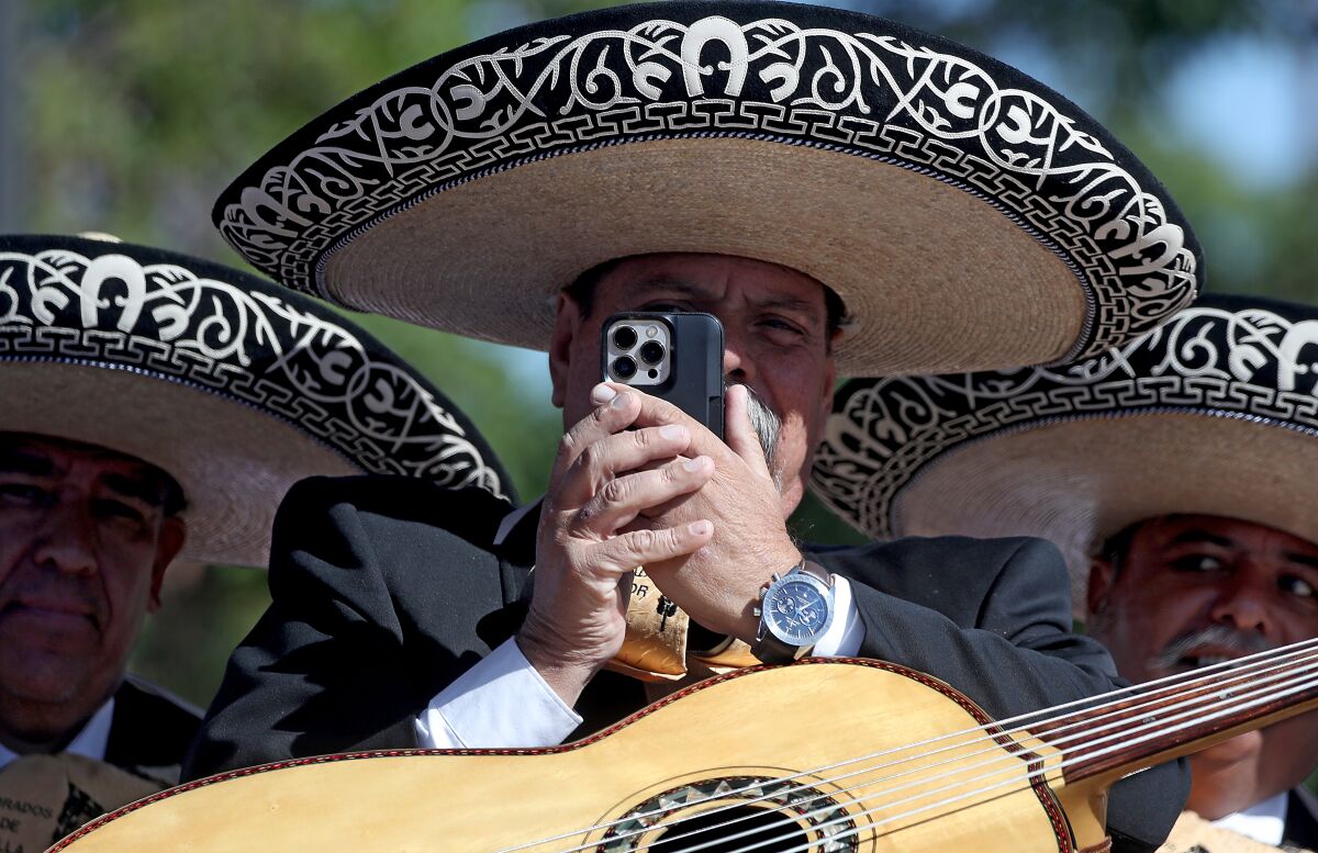 A mariachi musician takes a photograph with his phone during a campaign event in Mariachi Plaza.