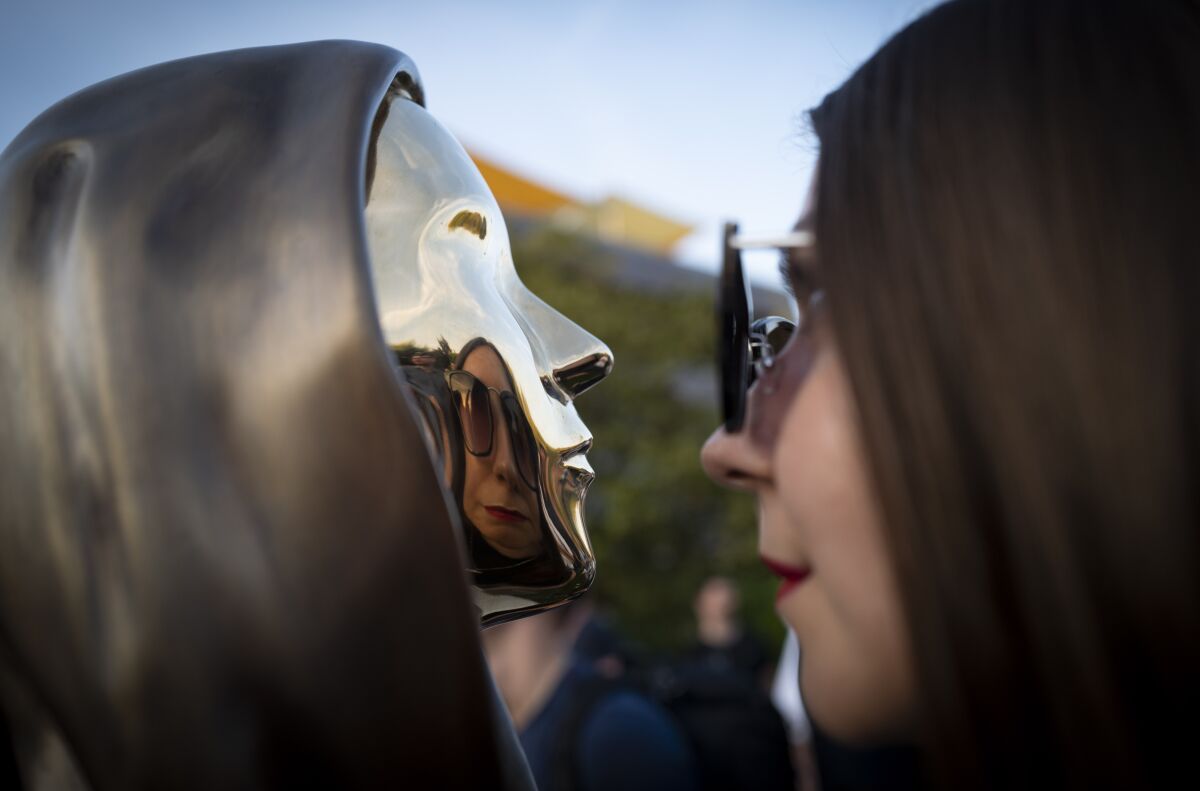 A woman looks at her reflection in a newly unveiled statue of the mysterious developer of the Bitcoin digital currency in Budapest, Hungary, Thursday, Sept. 16, 2021. A bronze statue was unveiled in Hungary’s capital on Thursday which its creators say is the first in the world to pay homage to the anonymous creator of the Bitcoin digital currency. Erected in a business park near the Danube River in Budapest, the bust sits atop a stone plinth engraved with the name of Satoshi Nakamoto, the pseudonym of the mysterious developer of Bitcoin whose true identity is unknown. (AP Photo/Bela Szandelszky)