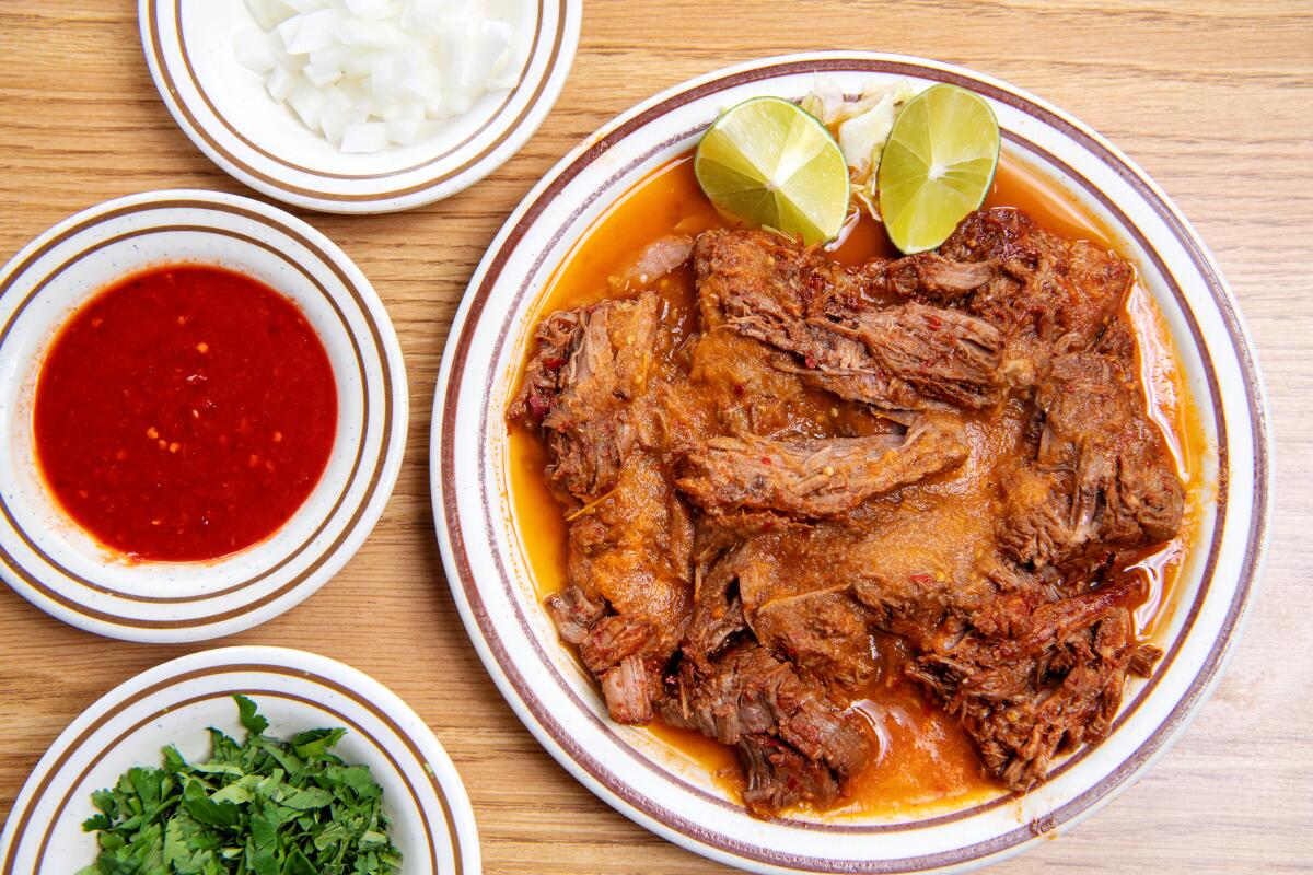 Birria de res on a white plate with garnishes and salsas next to it
