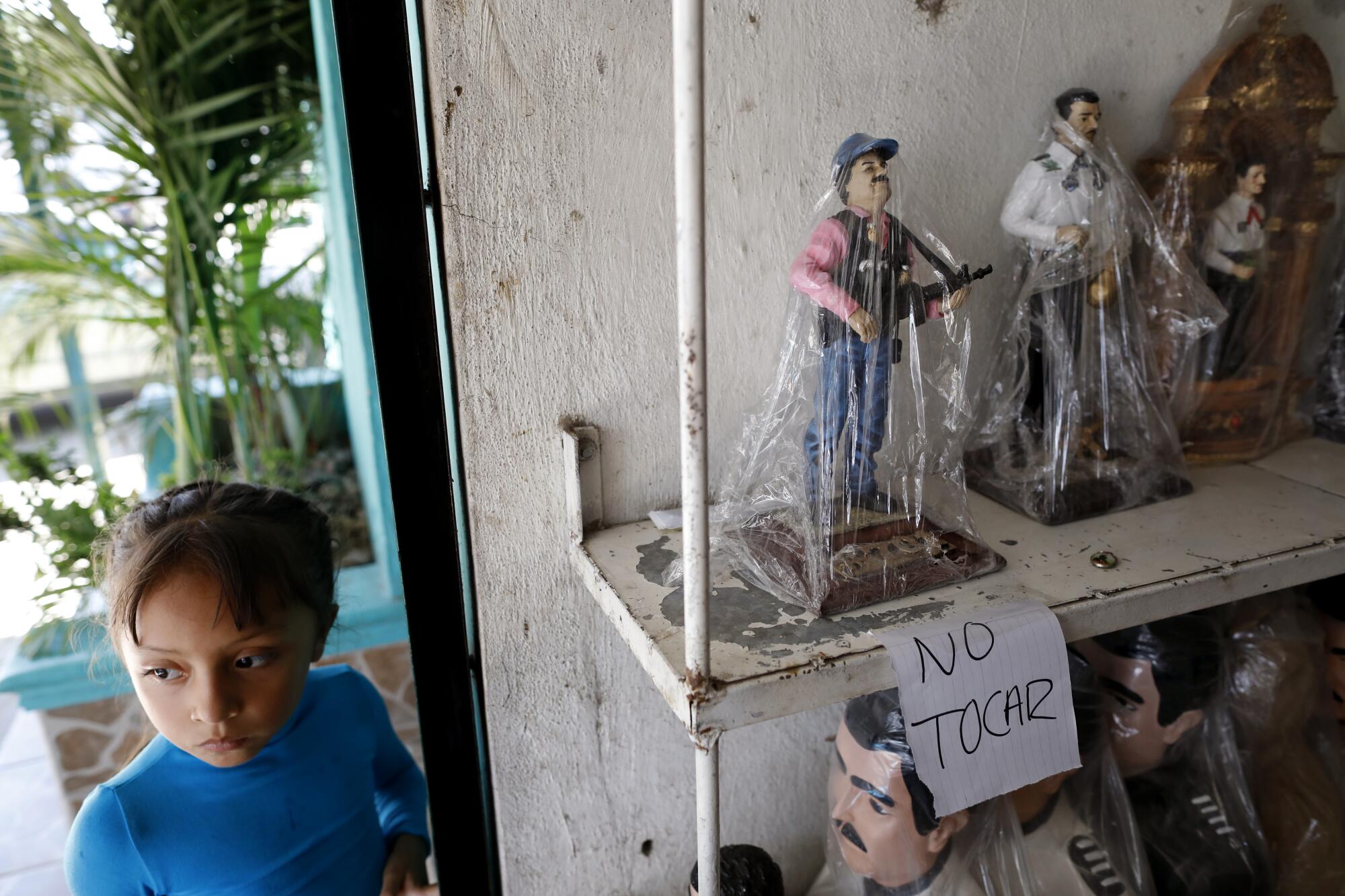  A child standing beside shelves holding plastic-wrapped figures of Joaquín "El Chapo" Guzman