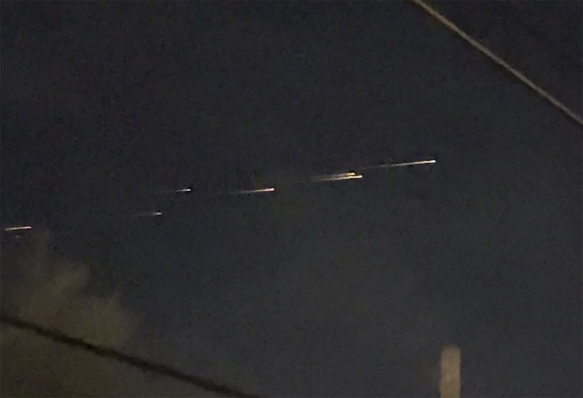 A row of seven streaks of light travel across the sky