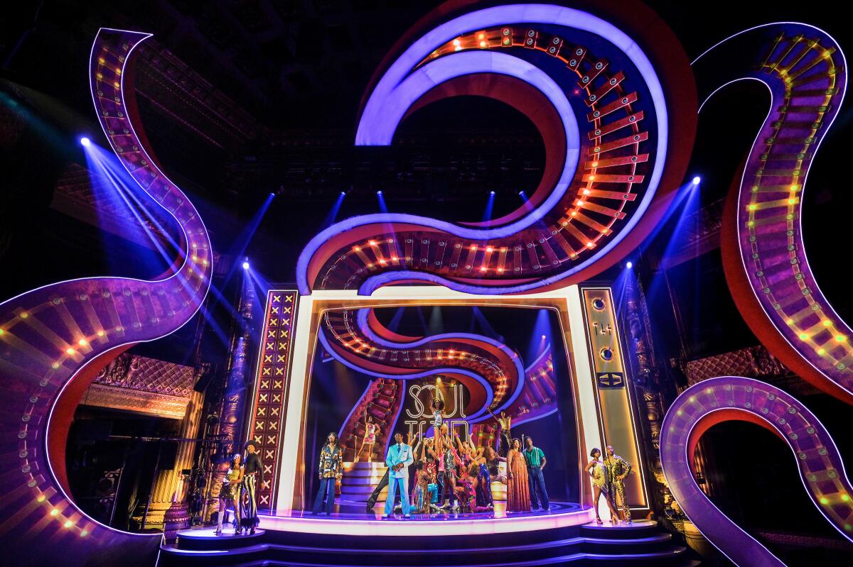 Actors perform on a stage set resembling a TV set and surrounded by swirls of neon lights