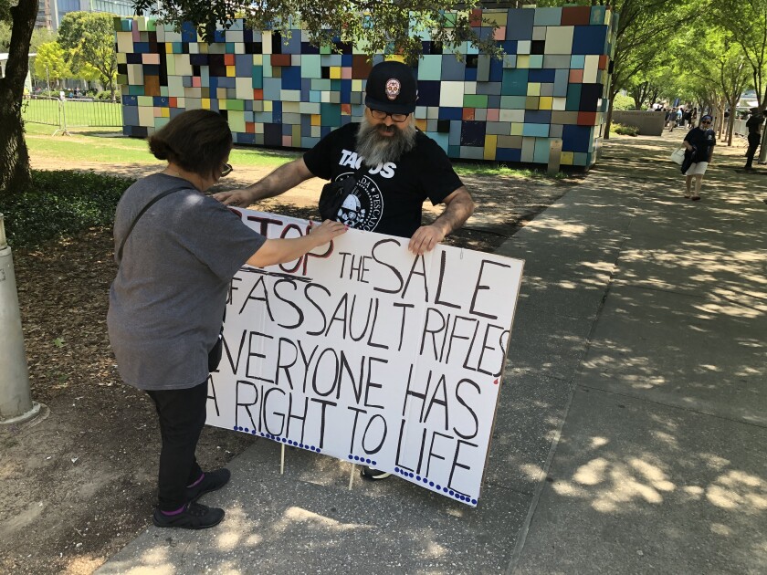A woman and man hold a sign opposing the sale of assault weapons