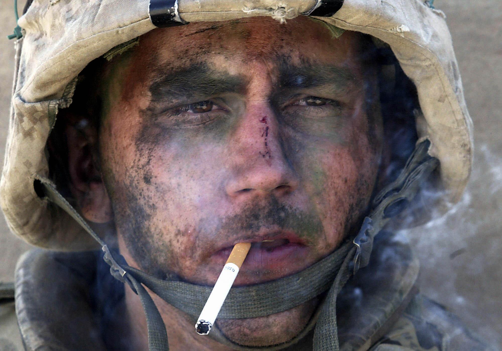 A closeup of a Marine smoking a cigarette, his face covered in dirt