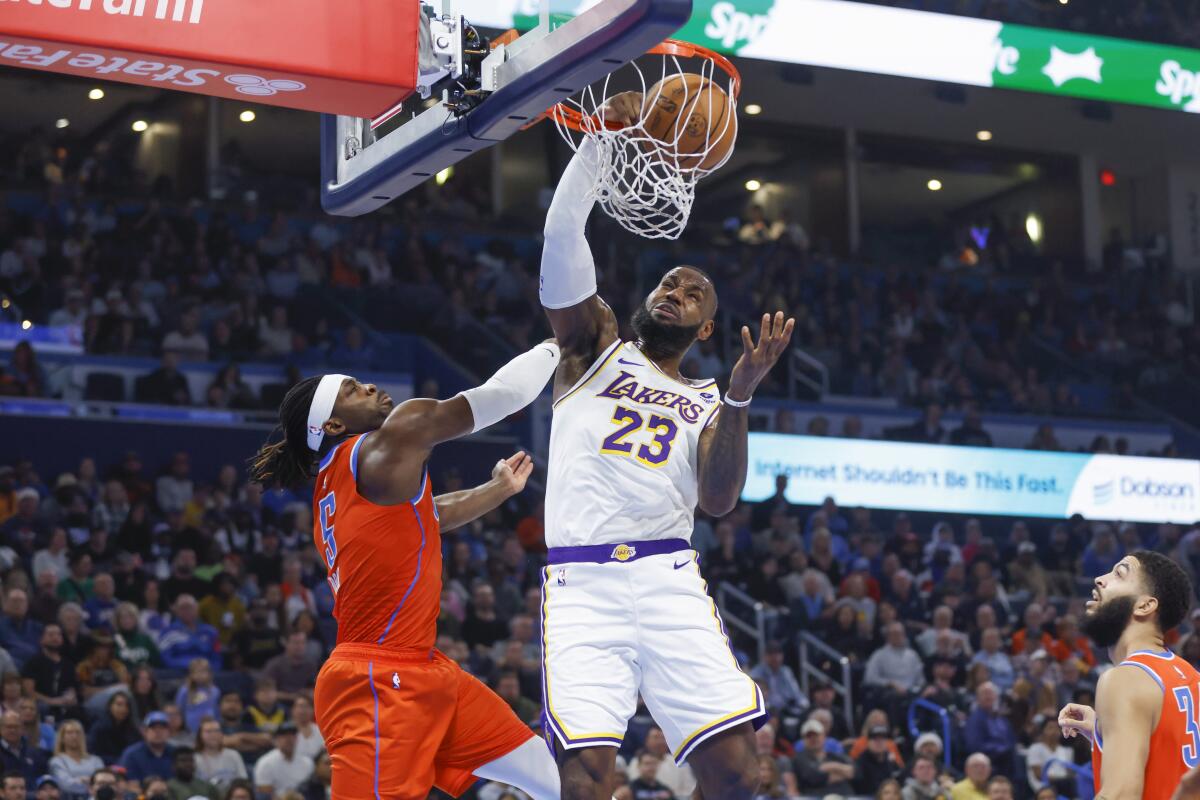 Lakers forward LeBron James dunks in front of Thunder guard Luguentz Dort, left, and forward Kenrich Williams, right.