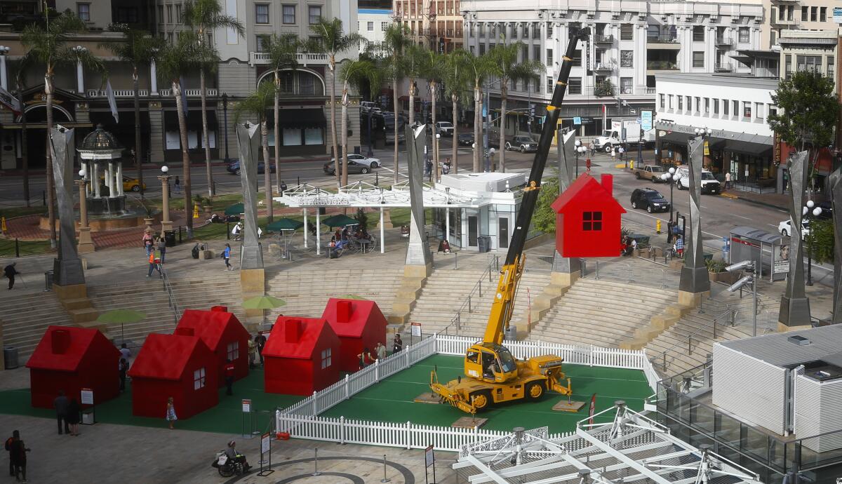 At Horton Plaza Park the art project Model Home created and designed by Mimi Lien is hoisted up sixty eight feet by a crane and then slowly spun to music. Below are five other homes of similar construction where the public is invited to peak into the homes.
