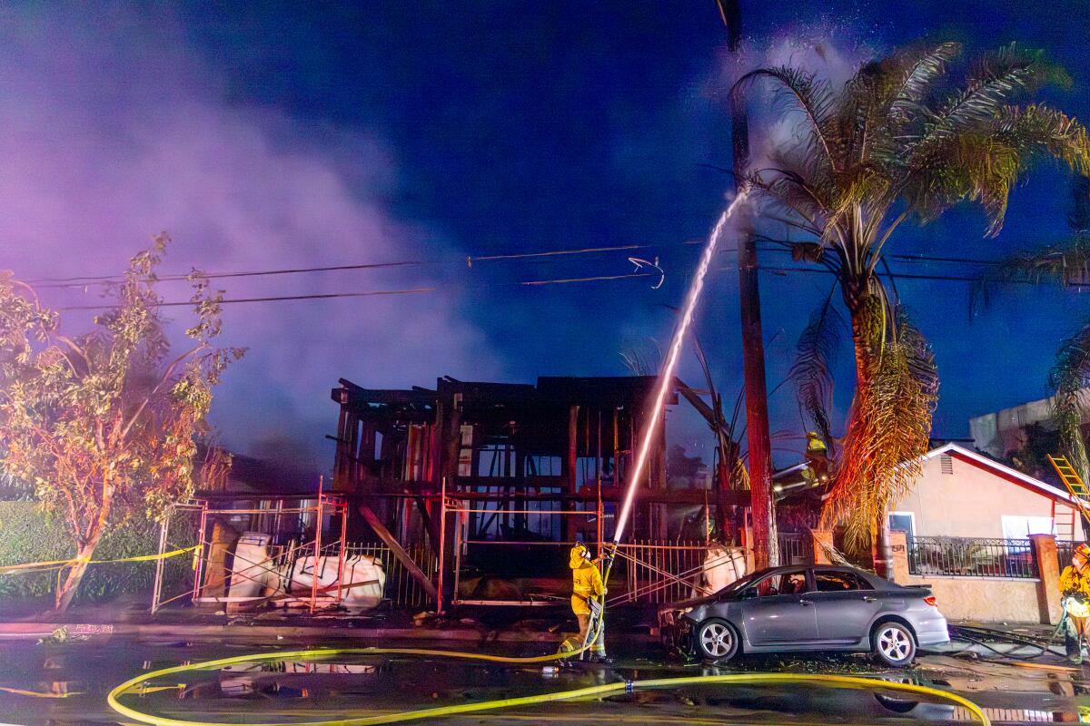 A firefighter sprays water from a hose onto a palm tree next to smoldering wooden framing at an apartment construction site