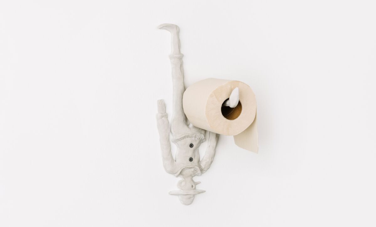 An upside down toy figure painted white holds a roll of toilet paper with an extended leg