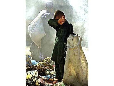 In a smoldering trash heap, 7-yr-old Issa rubs his burning eyes with the sleeve of his shalwar kamiz.