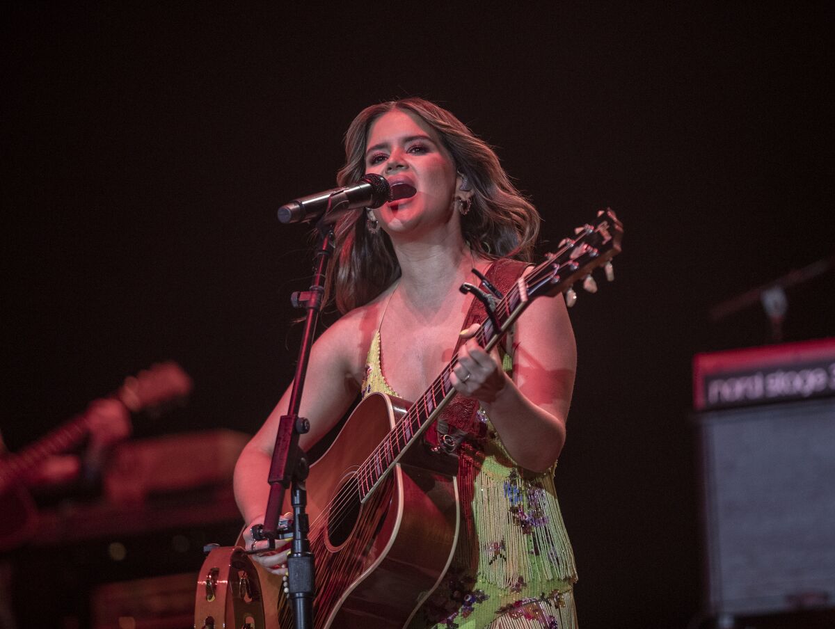 A female country music singer plays acoustic guitar and performs onstage.