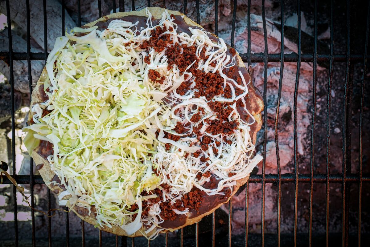 Closeup of a tortilla covered with meat, cheese and cabbage on top of a grill.