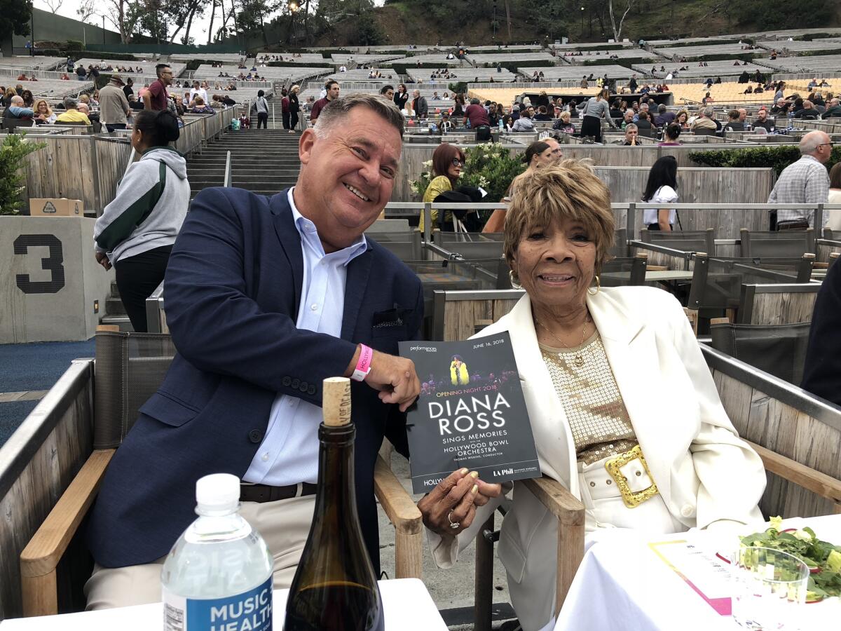 A man and a woman sit in box seats at the Hollywood Bowl holding a program with Diana Ross on the cover.